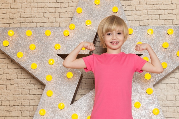 Free photo a front view cute little kid in pink t-shirt grey jeans on the star designed yellow stand and light background