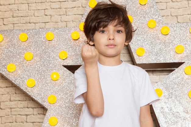 Free photo a front view cute little kid in white t-shirt dark jeans on the star designed yellow stand and light background