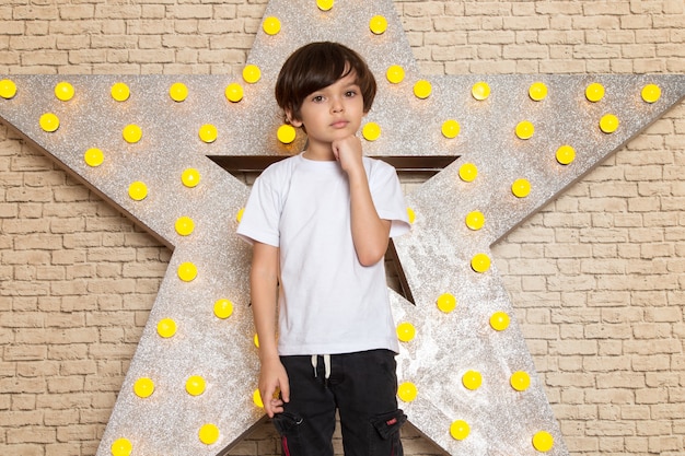 Free photo a front view cute little kid in white t-shirt dark jeans on the star designed yellow stand and light background