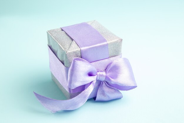 Front view cute little present tied with purple bow on blue floor