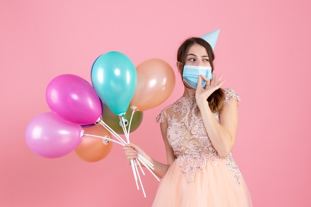 Front view cute party girl with party cap holding colorful balloons