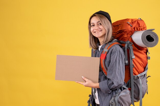 Front view of cute traveler girl with red backpack holding cardboard