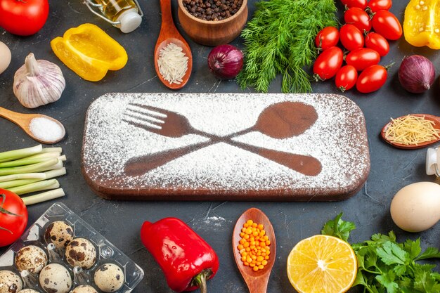 Front view of cutting board with flour drawn fork knife among fresh vegetables different spices green bundles