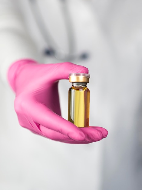 Front view of defocused doctor with surgical glove holding vaccine