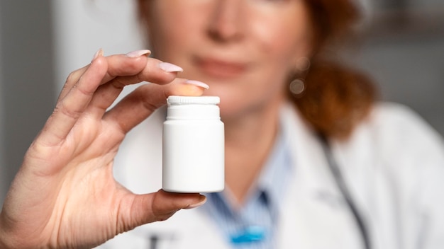 Front view of defocused female physician holding bottle of medicine