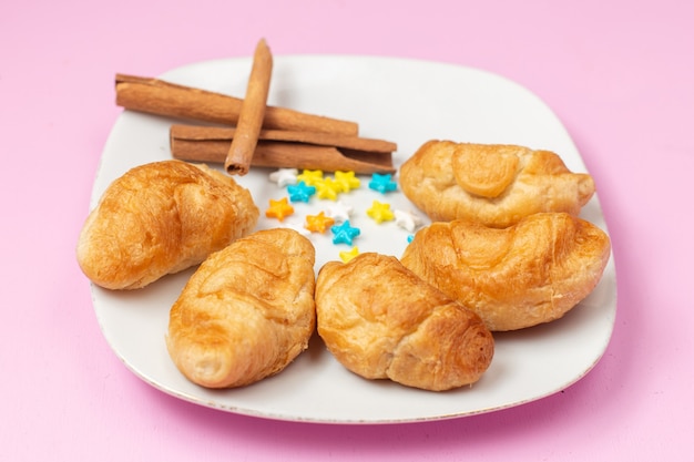 Free photo front view delicious baked croissants with fruit filling inside with cinnamon candies on the pink background