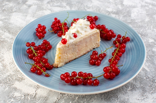 Free photo front view of delicious cake slice inside blue round plate with cream and red cranberries on the grey desk