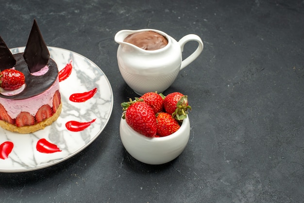 Front view delicious cake with strawberry and chocolate on oval plate bowl of strawberries