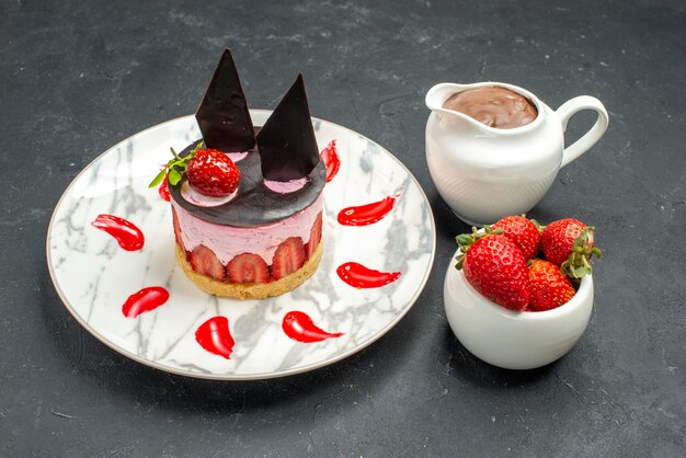 Front view delicious cheesecake with strawberry and chocolate bowl of strawberries and chocolate on oval plate on dark background