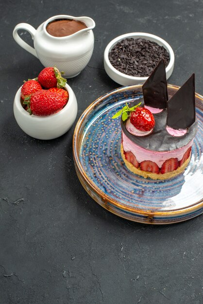 Front view delicious cheesecake with strawberry and chocolate on oval plate bowls with strawberries chocolate on dark