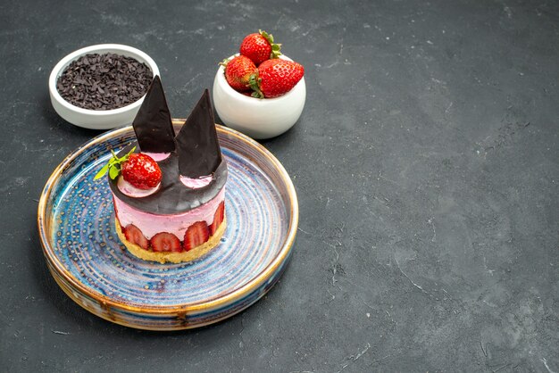 Front view delicious cheesecake with strawberry and chocolate on plate bowls with strawberries chocolate on dark isolated background with copy place