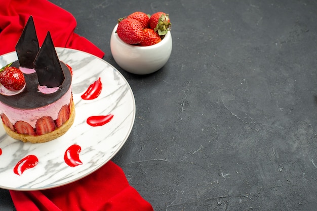 Free photo front view delicious cheesecake with strawberry and chocolate on plate red shawl bowl with strawberries on dark isolated background free place