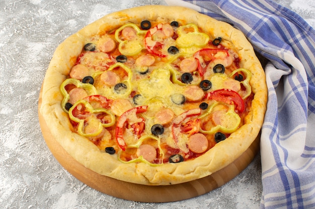 Front view of delicious cheesy pizza with olives sausages and tomatoes on the grey desk