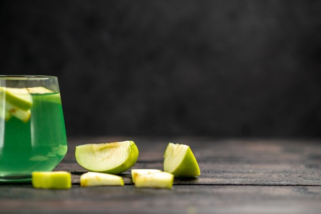 Front view of delicious juice in a glass and an chopped apple on dark background