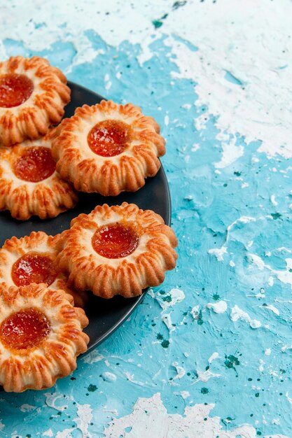 Front view delicious little cookies with jam inside black plate on blue desk cookie biscuit sweet sugar color tea