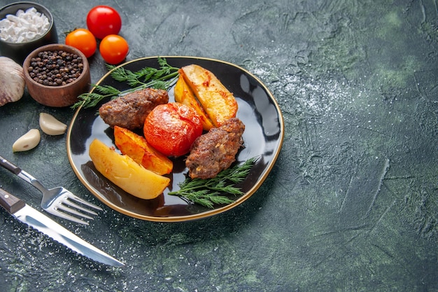 Free photo front view of delicious meat cutlets baked with potatoes and tomatoes on a black plate cutlery set spices garlics tomatoes on the right side