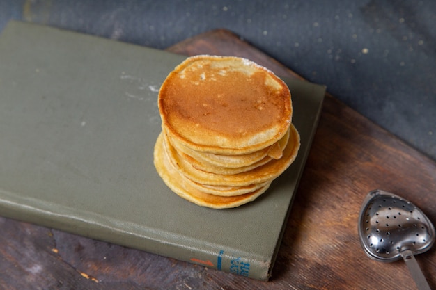 Front view of delicious pancakes on the copybook wooden desk and grey surface