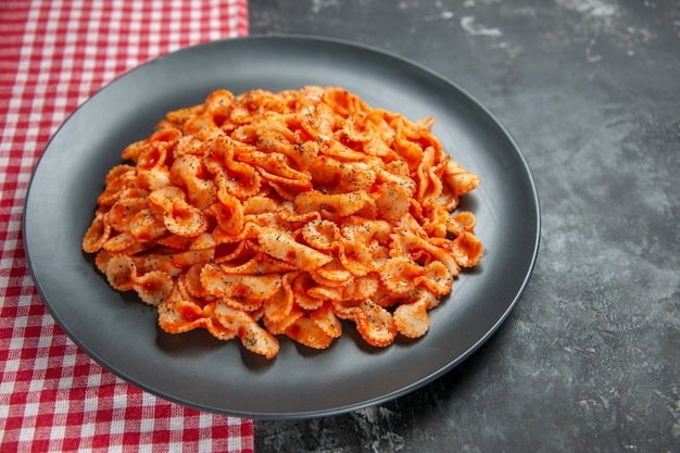 Front view of delicious pasta meal on a black plate for dinner on a red stripped towel on dark background