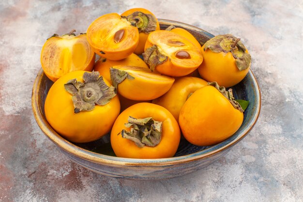 Front view delicious persimmons in a bowl on nude background