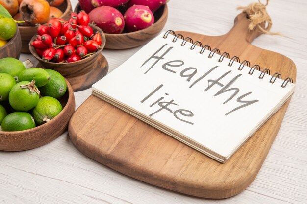 Front view different fresh fruits inside plates with notepad on white background color tropical healthy life exotic berry tree ripe