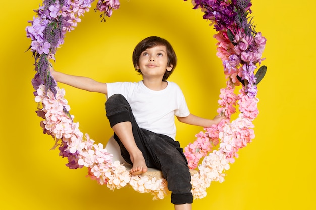 A front view dreaming cute boy in white t-shirt around flower stand on the yellow desk