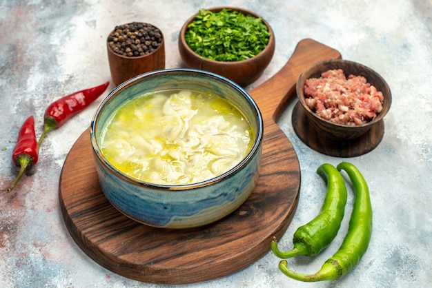 Free photo front view dushbara on chopping board bowls with meat greens black pepper hot peppers on nude background