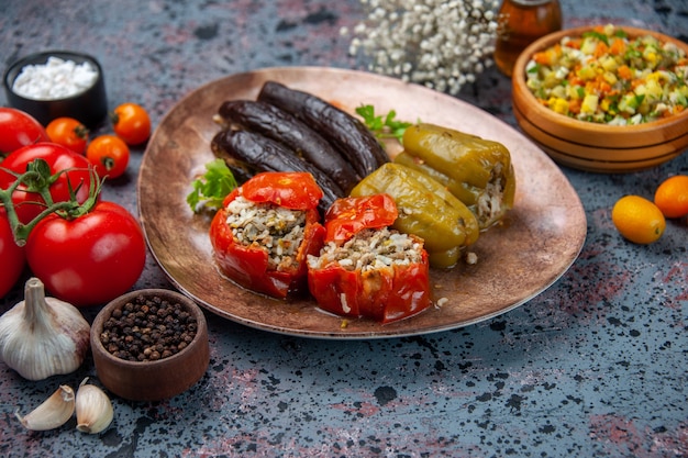 front view eggplant dolma with cooked tomatoes and bell-peppers filled with ground meat inside plate on a blue background