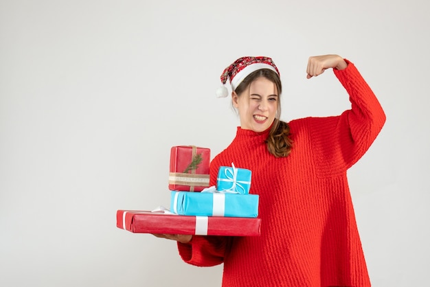 Free photo front view elated girl with santa hat holding her xmas gifts showing muscle