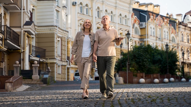 Front view of elder couple out for a walk in the city with tablet