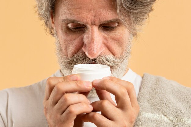 Front view of elder man with beard smelling moisturizer