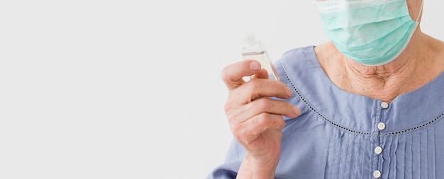 Front view of elder woman wearing medical mask and holding hand sanitizer