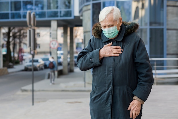 Front view of elder woman with medical mask feeling ill while in the city