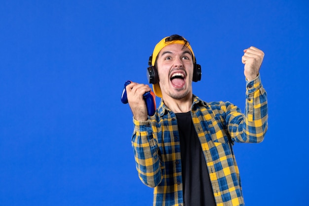 Front view of emotional male gamer with gamepad playing video game on blue wall