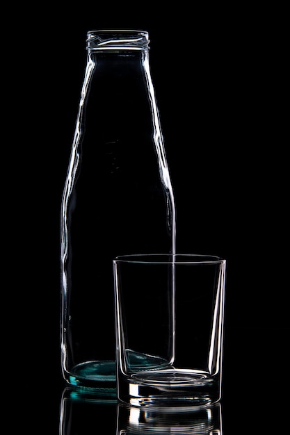 Front view of empty bottle and a glass on black background with free space