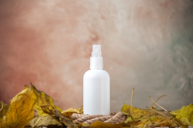 Front view empty spray bottle around fall leaves on nude background