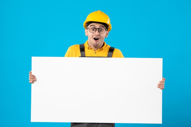 Free Photo front view of excited male builder in yellow uniform with plan blue wall