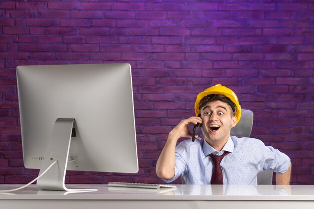 Front view excited male constructor behind office desk talking at phone