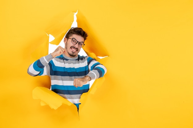 Free photo front view excited young man looking through ripped paper yellow wall