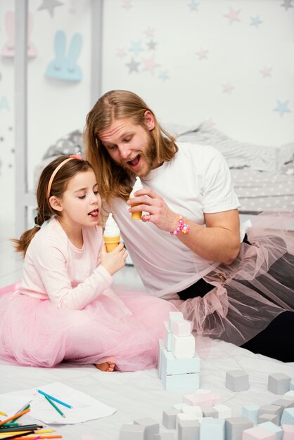 Front view of father and daughter in tutu skirts eating ice creams