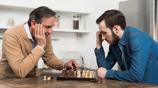 Front view father and son playing chess in kithcen