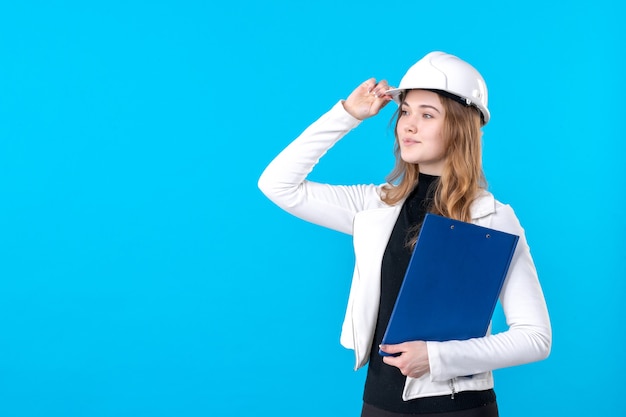 Free photo front view female architect in helmet holding blue file plan on blue