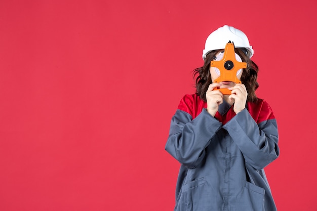 Free photo front view of female architect in uniform with hard hat holding measuring tape in front of her face on isolated red wall