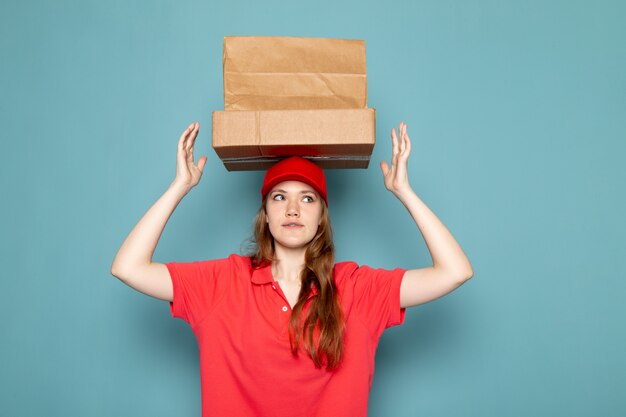 Free Photo a front view female attractive courier in red polo shirt red cap holding brown packages above her head posing on the blue background food service job