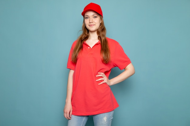 Free Photo a front view female attractive courier in red polo shirt red cap and jeans posing on the blue background food service job