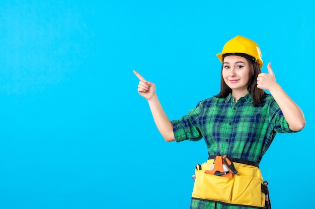 Front view female builder in uniform and helmet smiling on blue