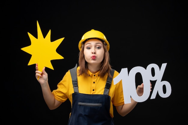 Free photo front view female builder in uniform holding yellow figure and on black wall