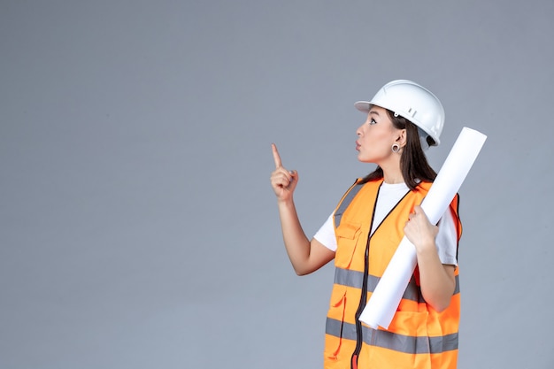 Front view of female builder in uniform with poster in her hands on gray wall