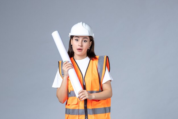 Front view of female builder in uniform with poster in her hands on white wall