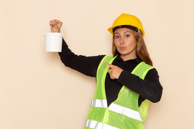 Front view female builder in yellow helmet black shirt holding can of paint on white wall female builder  architect