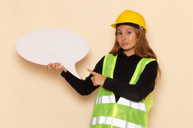 Front view female builder in yellow helmet holding a big white sign on white wall female builder construction architect